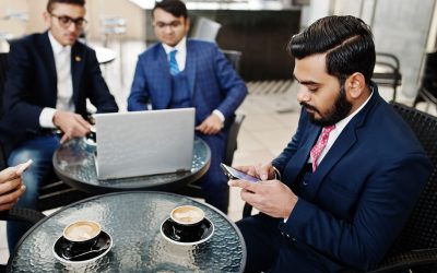 Group of indian business man in suits sitting at office on cafe with laptop, texting on phones and making photo of coffee.